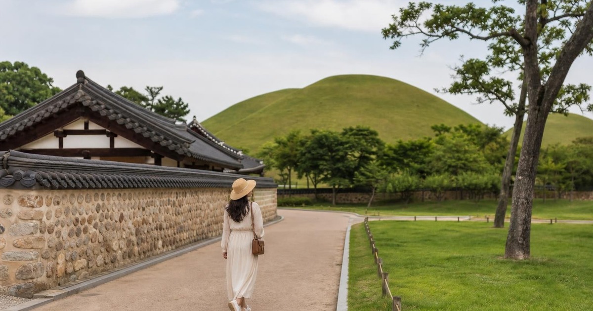 Traveler walking near Gyeongju royal tomb mounds with traditional roofs in the distance.
