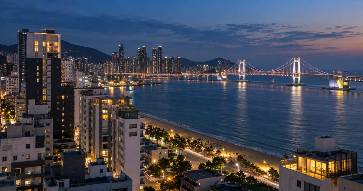 Evening view over a Busan coastal district with a lit bridge across the bay and hotels near the beach.
